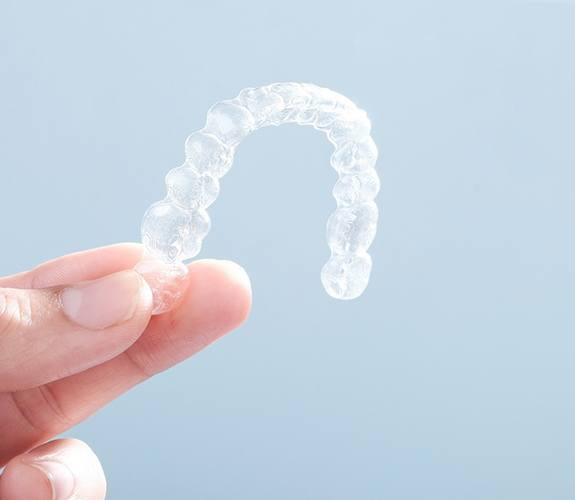 Fingers holding a clear aligner