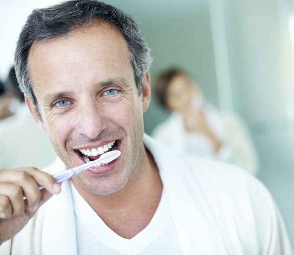 Man smiling while brushing his teeth