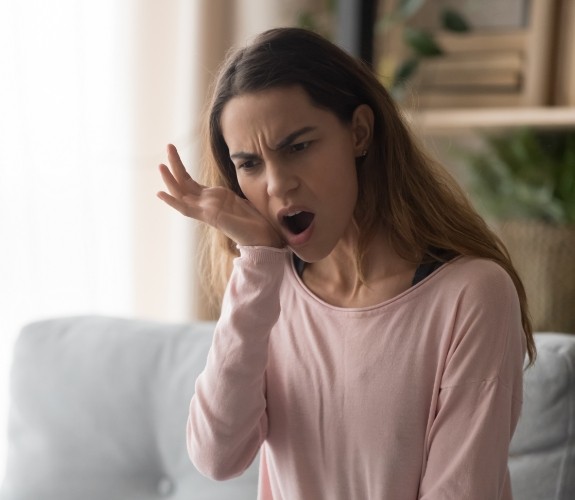 Woman sitting on couch and touching her cheek in pain