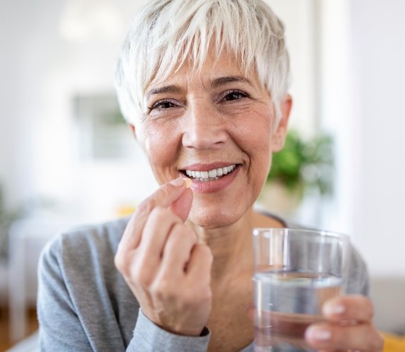 Senior woman holding pill and glass of water