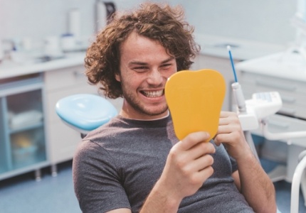 Man in dental chair admiring his smile in mirror after dental services